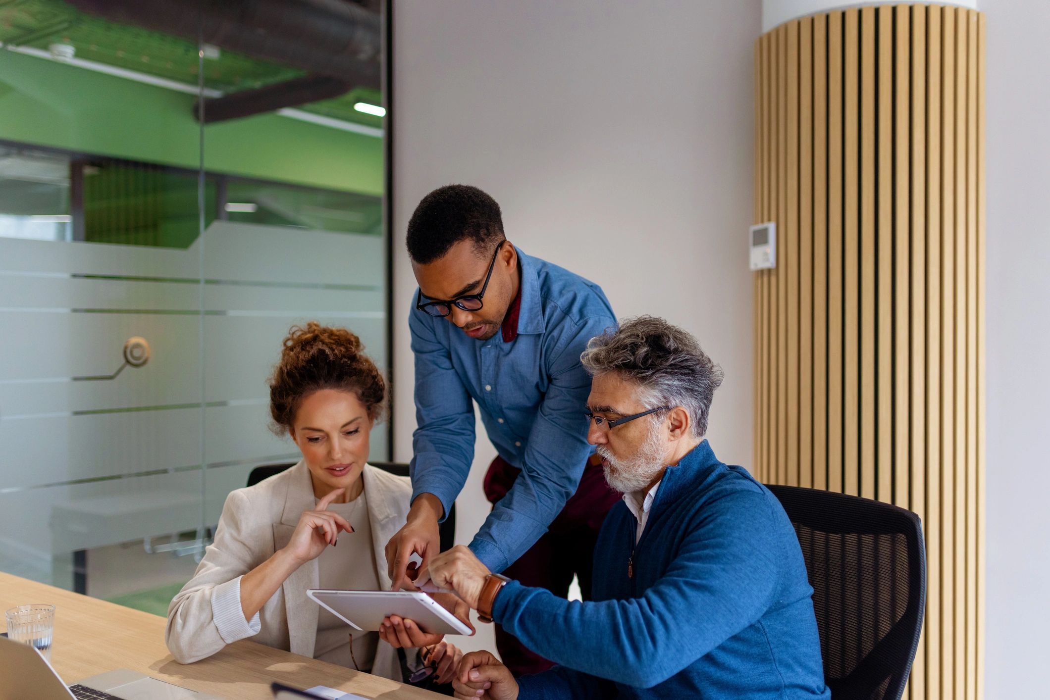Three business professionals collaborating on a tablet in a modern office.